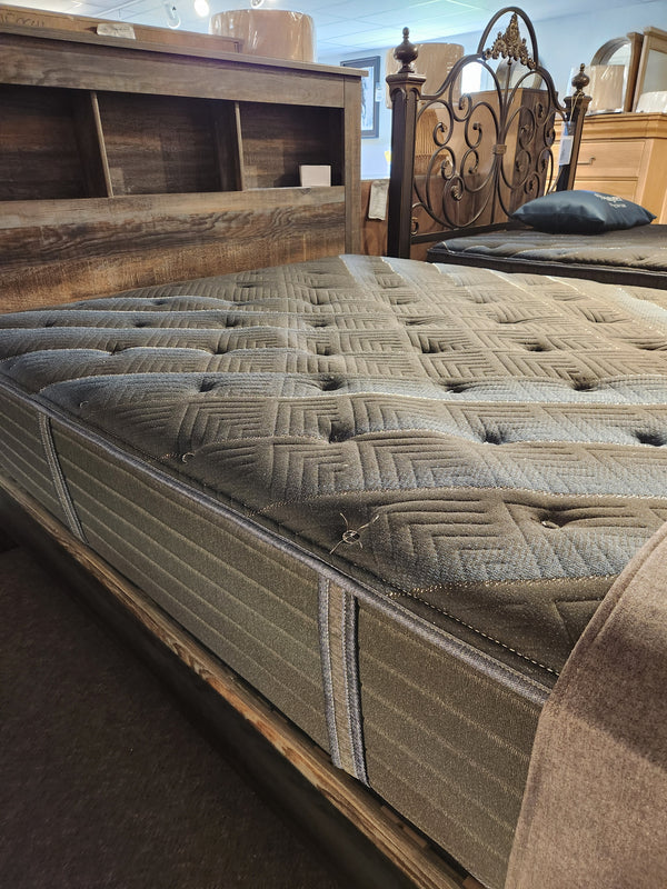 A close-up of a Beauty-rest Haven TT Firm Mattress by Beauty-rest on a wooden bed frame in a showroom.
