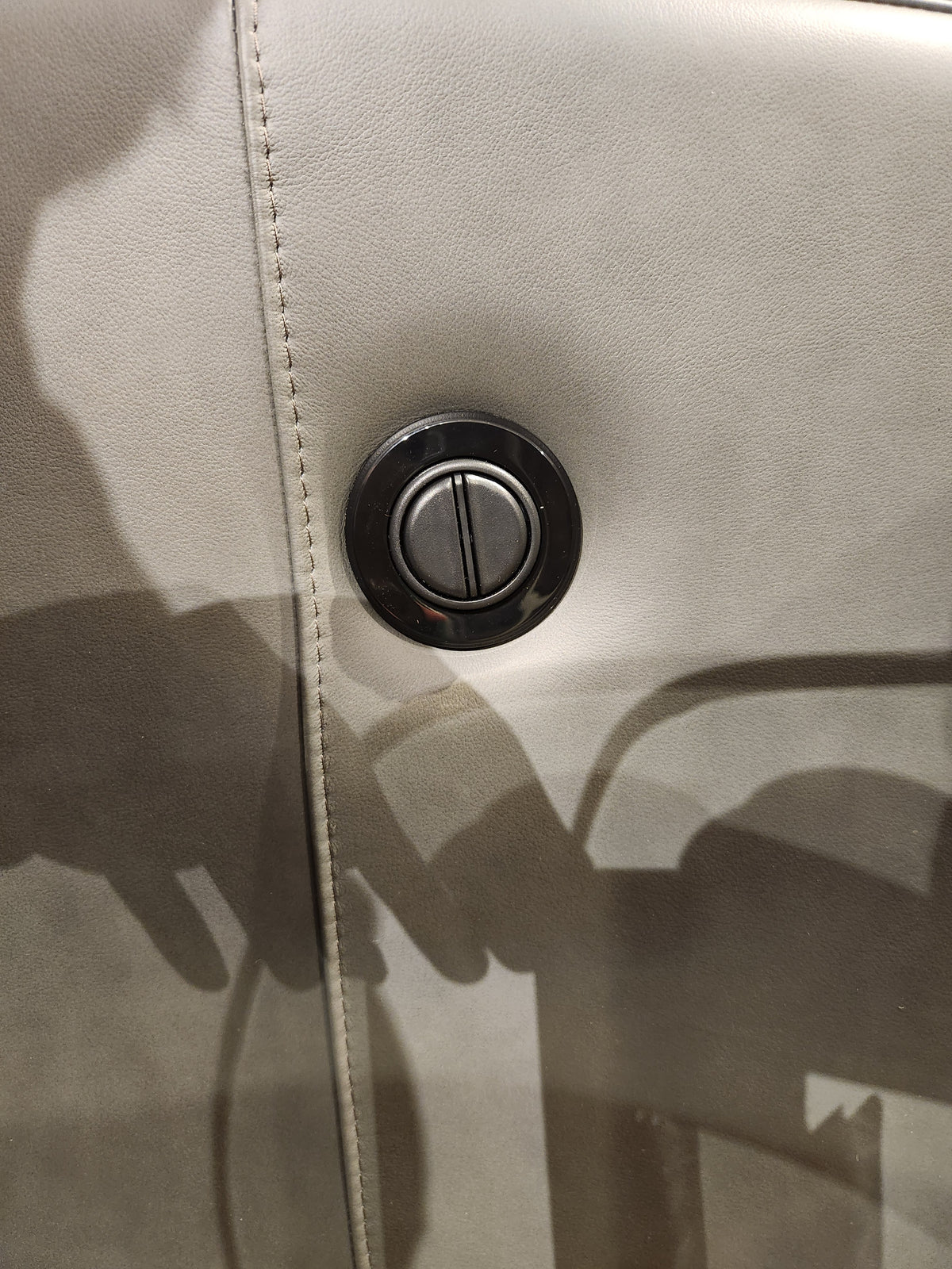 Close-up of a round button on the grey Leather Craft Texas Power Reclining Loveseat, showing stitching and shadows.