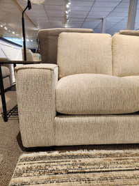 The Leather Craft Mesa Loveseat offers luxurious comfort with wide armrests, shown on a patterned rug in the showroom.