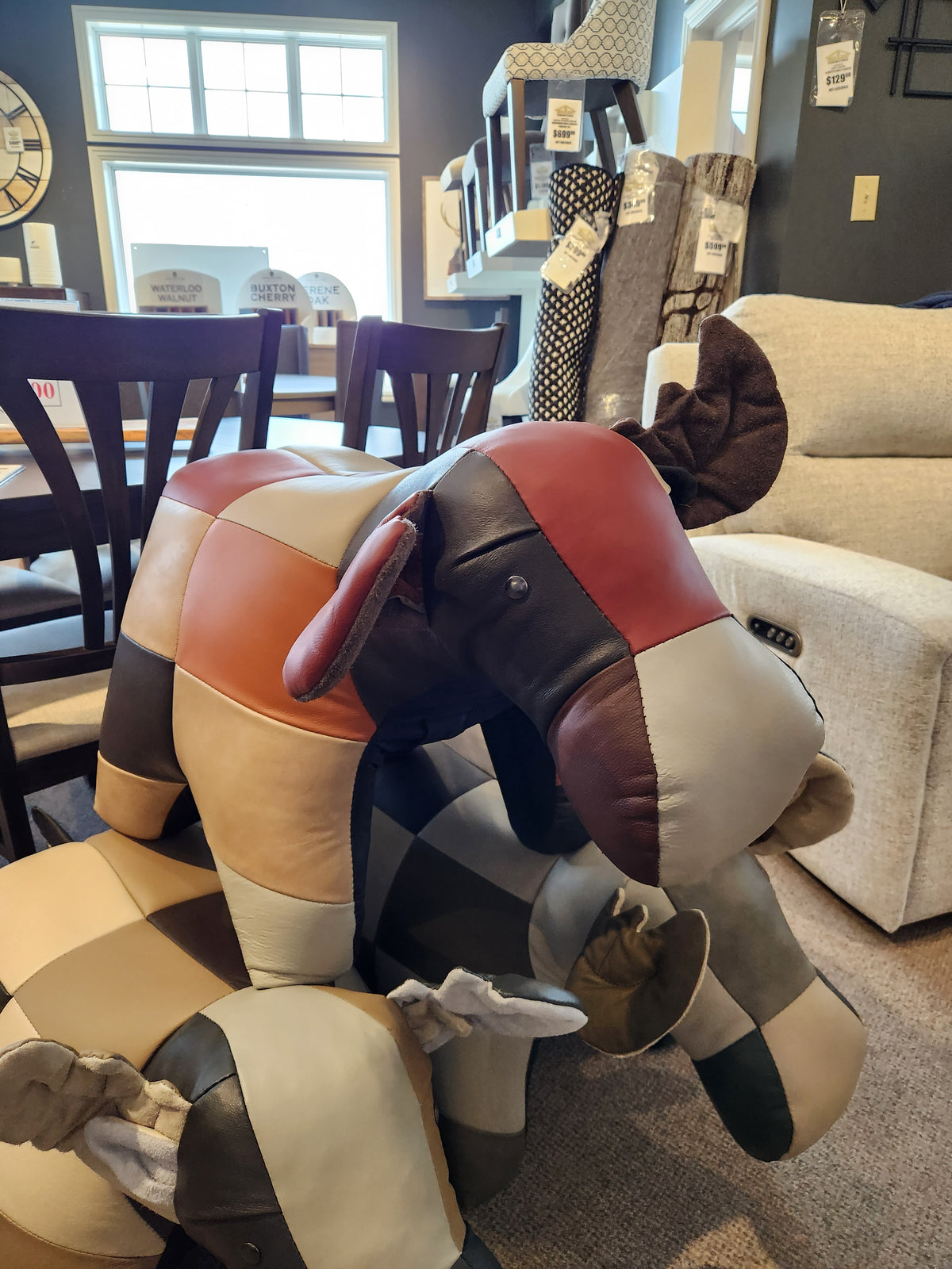 Two Reiner's Originals Leather Moose Ottomans are showcased in a furniture store among chairs and decor items.