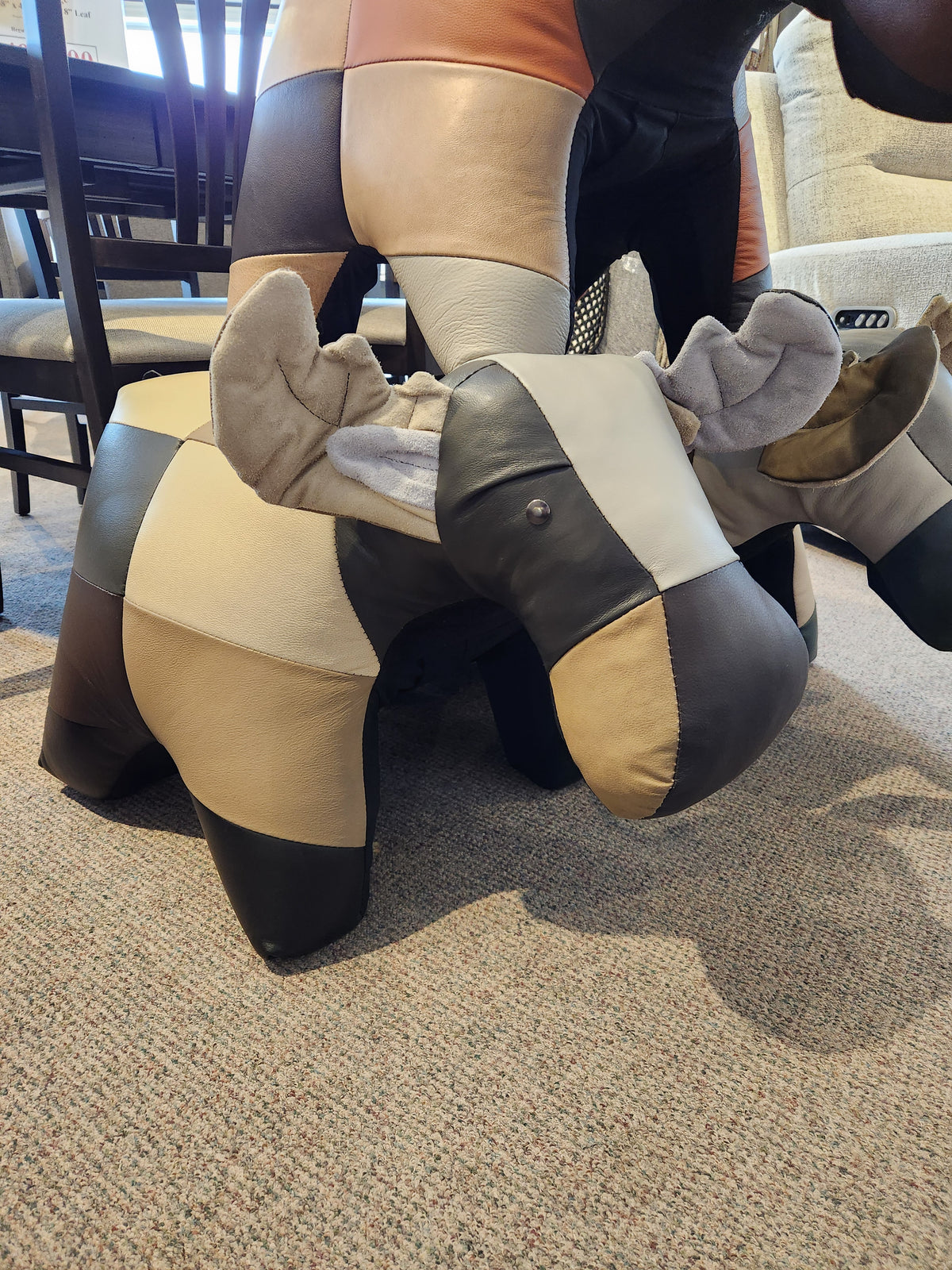 A Reiner's Originals Reiner's Leather Animal Ottoman--Moose with horns sits on a carpeted floor in a furniture store.