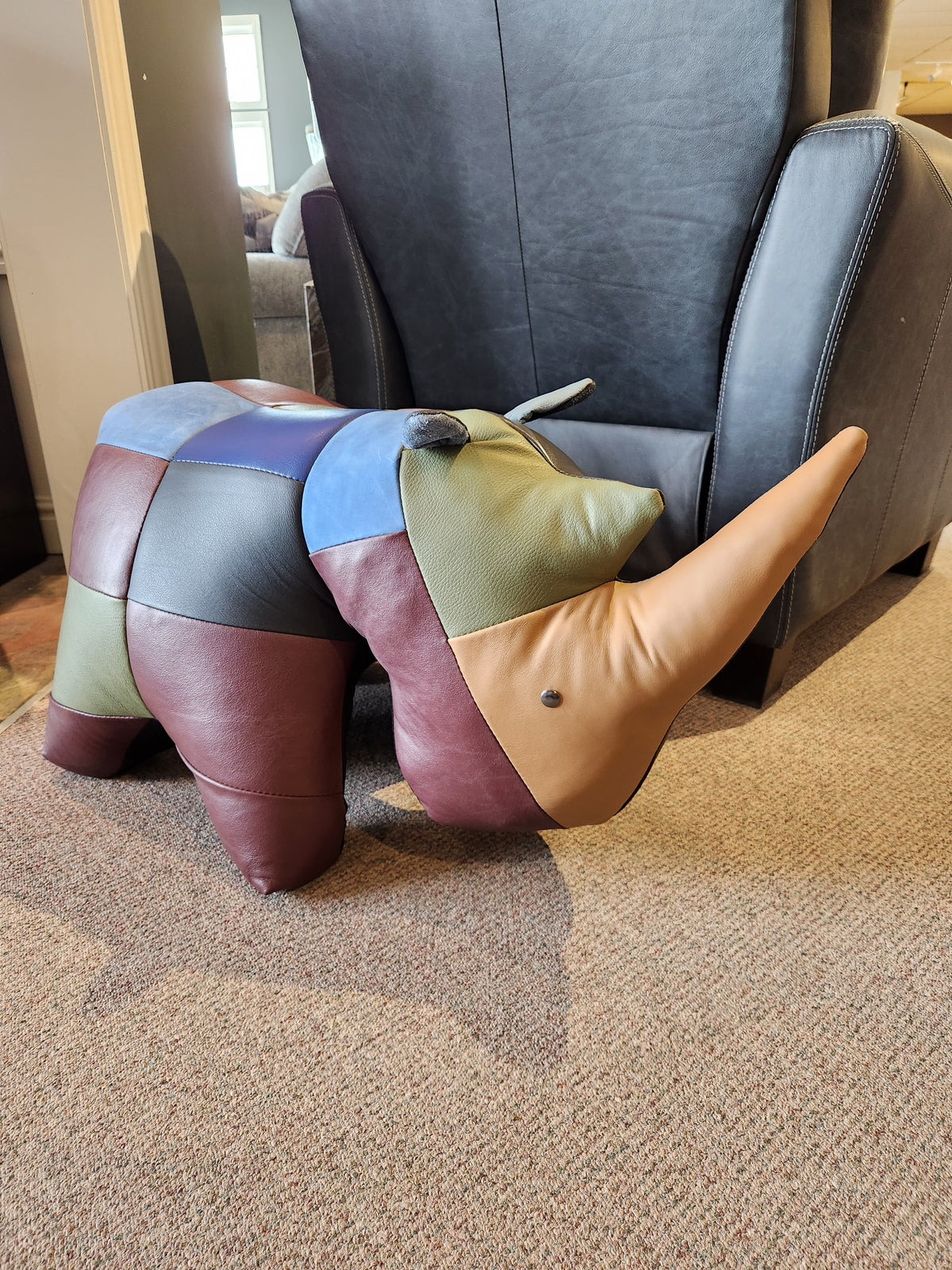 Reiner's Originals Reiner's Leather Animal Ottomans-- Rhino sits on the carpet in front of a black armchair.