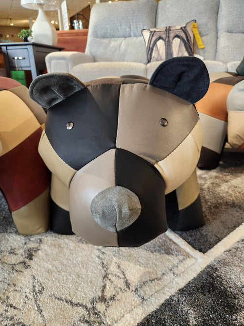 A Reiner's Originals Reiner's Leather Animal Ottomans-- Bear sits on a patterned rug in a furniture showroom.