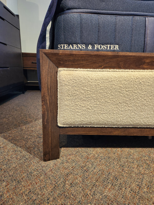 Corner of a Magnussen B5907 Llewellyn Queen Upholstered Bed Frame with a "Stearns & Foster" mattress on carpet.