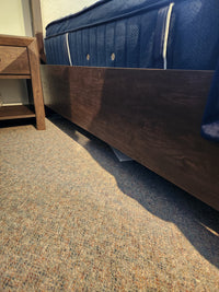 A paper lies on Merino Pearl carpet beneath a Magnussen B5907 Llewellyn Queen Bed Frame next to a nightstand.