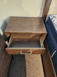The Magnussen Llewellyn B5907 Night Stand with a walnut finish and single drawer is beside a bed with a blue mattress.