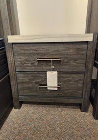 The Magnussen B5990 Plum Creek Night Stand with two drawers in Ravenwood Black stands on a carpeted floor.
