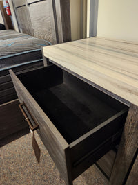 A close-up of an open B5990 Plum Creek Night Stand by Magnussen in Ravenwood Black, showing its empty drawer.