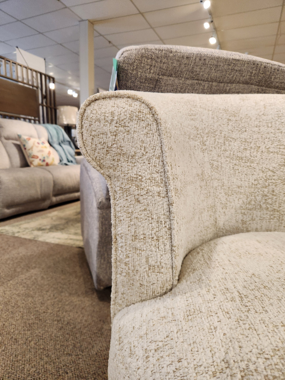 Close-up of the beige Attica Swivel Chair by Best in a showroom, with sofas and fabric samples in the background.