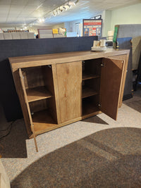 The Nia Sideboard by Donald Choi features adjustable shelves and open cabinet doors, shown in a furniture showroom.