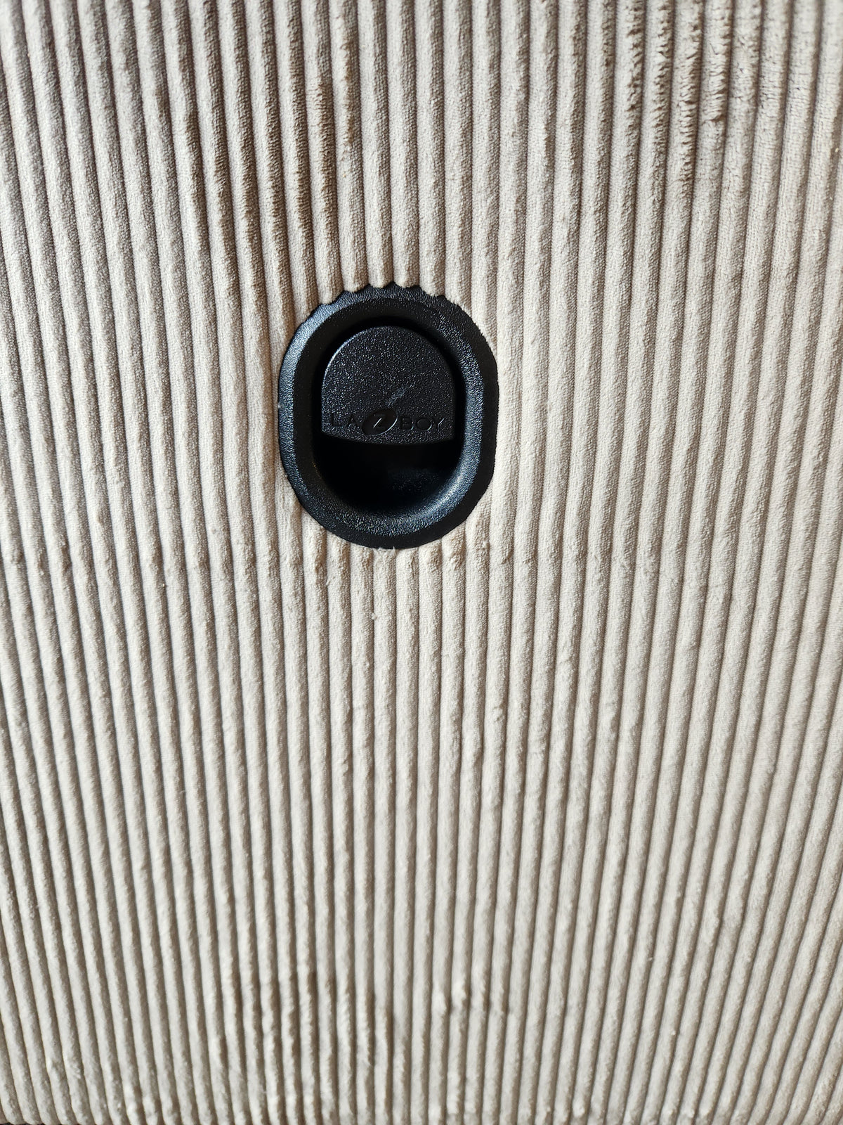 Close-up of a black recessed handle on the 761 Joel Reclining Loveseat by La-z-boy, featuring a ribbed beige surface.