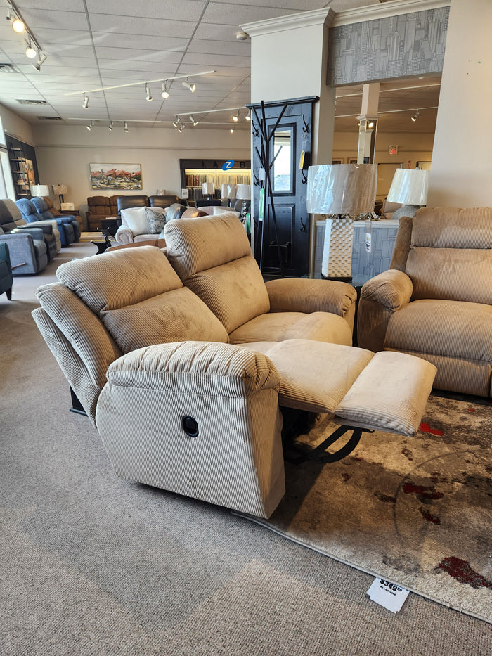 The La-z-boy 761 Joel Reclining Loveseat in beige is extended in a showroom, surrounded by sofas and lamps.