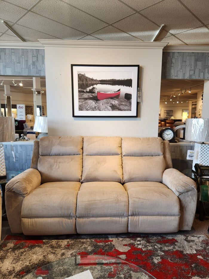 A La-z-boy 761 Joel Reclining Sofa in beige with cushioned arm pads sits below a framed canoe photo in the showroom.