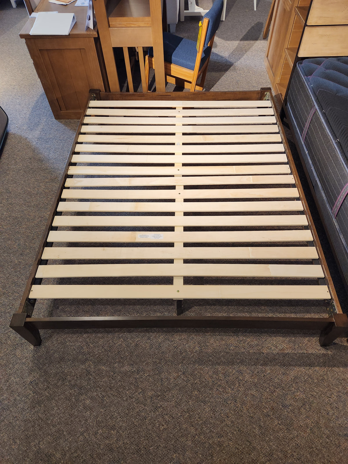 The Fashion Willa Queen Platform Bedframe features a minimalist wooden design with slatted base, displayed in a showroom.