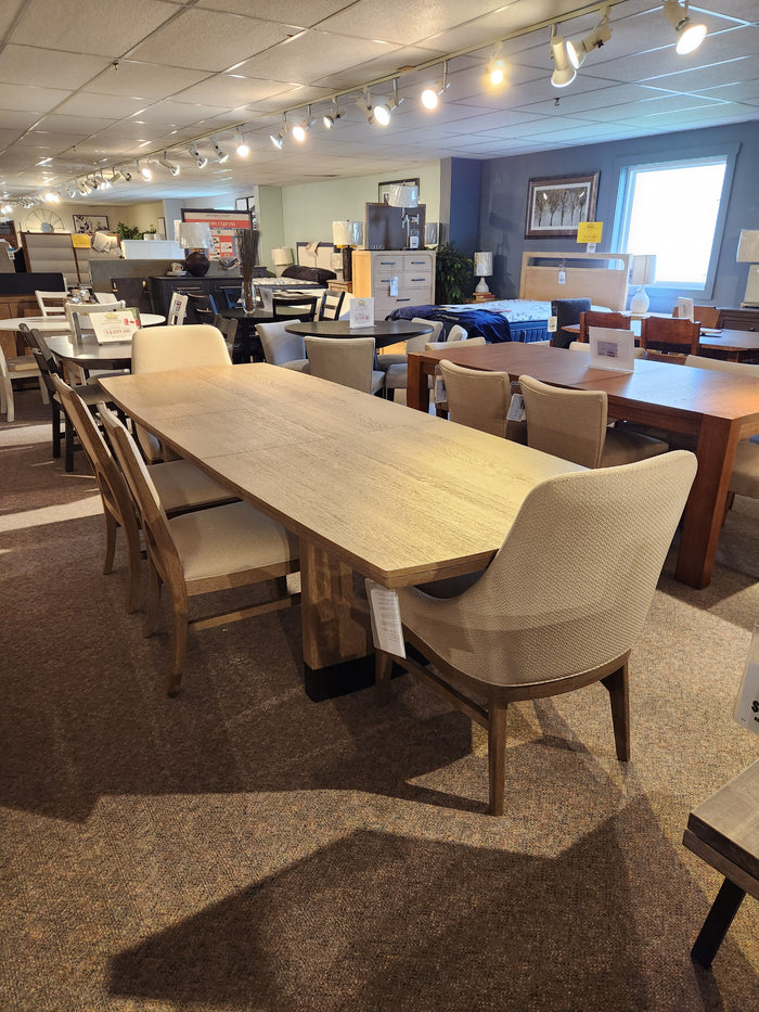 Magnussen D5878 Trestle 5 Piece Dining Package with honey wheat finish and six beige chairs in showroom display.
