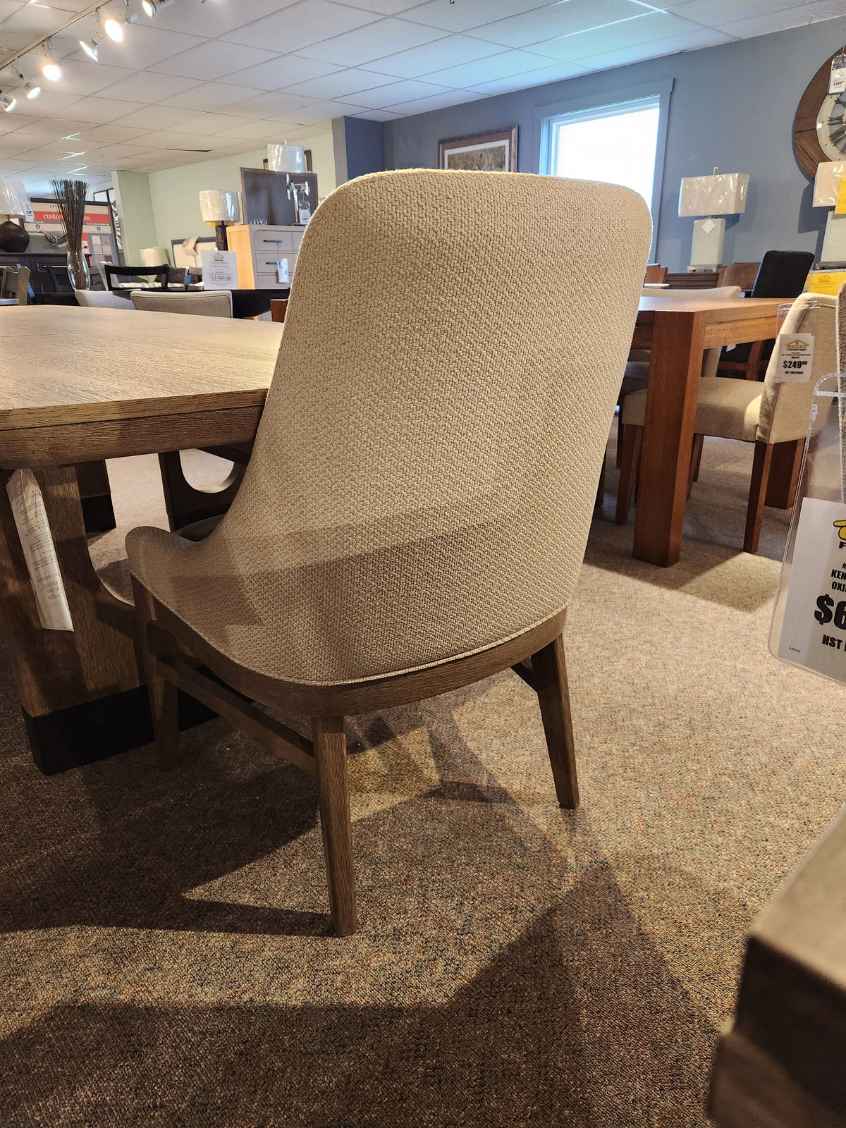 Beige upholstered chair with wooden legs from Magnussen’s D5878 Trestle 5 Piece Dining Package on display.