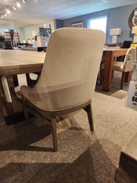 Beige upholstered chair with wooden legs from Magnussen’s D5878 Trestle 5 Piece Dining Package on display.