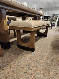 A Magnussen D5878 Trestle 5 Piece Dining Package with beige cushions sits on a carpeted showroom floor.