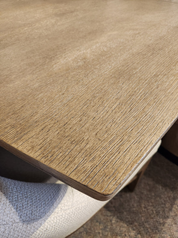 Close-up of the Magnussen D5878 Trestle 5 Piece Dining Package in Honey Wheat beside a light cushioned chair.