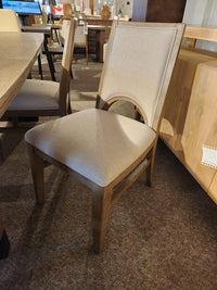 Magnussen D5878 Trestle 5 Piece Dining chair with beige upholstery, shown on a carpeted showroom floor.