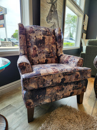 The Best Field & Stream Andrea Wing Back Chair with a nature motif sits on a wood floor by large living room windows.
