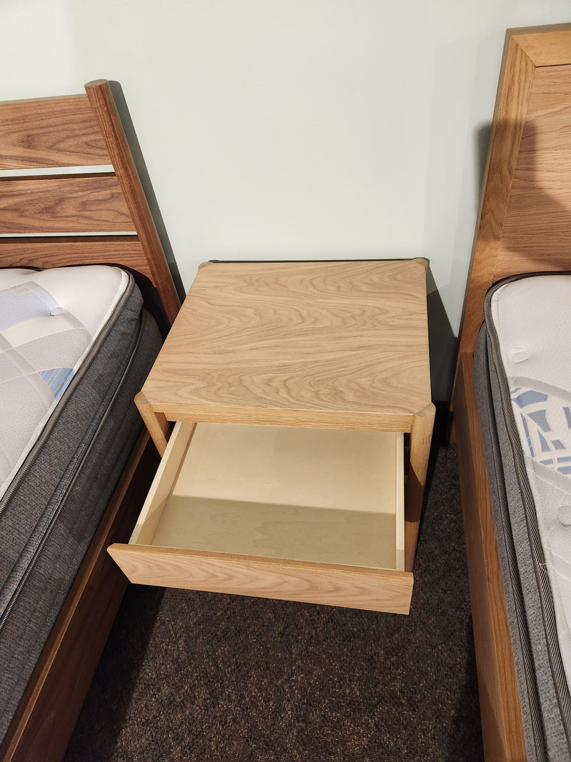 The Palliser EQ3 Monarch Single Drawer Nightstand in walnut sits between two beds with visible mattresses.