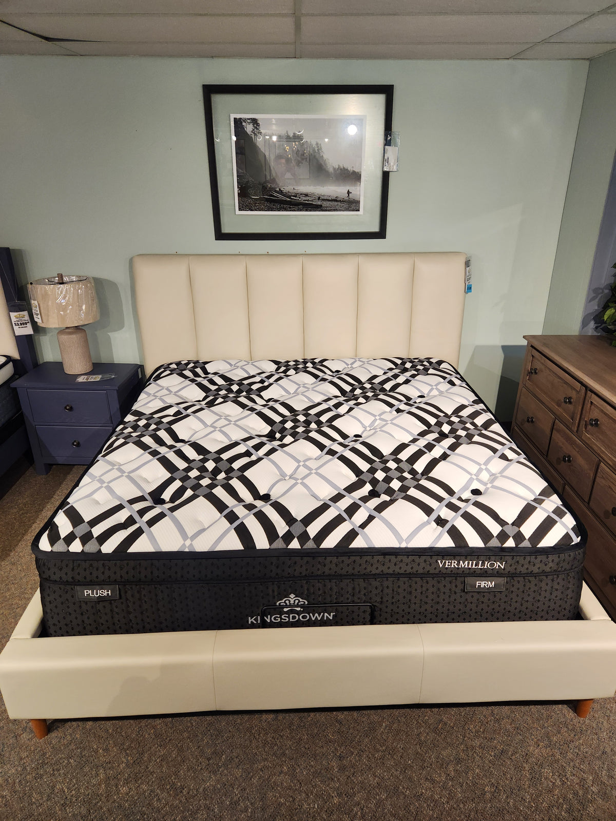 A KingsDown Vermillion ET Plush Mattress on a cream upholstered bed frame in a bedroom showroom.