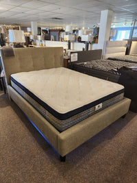 A KingsDown Garland ET Plush Mattress on a beige upholstered bed frame is displayed for a cooler sleep experience.