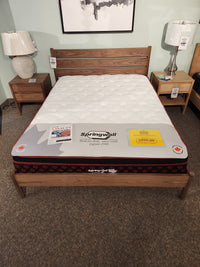 A Springwall Canada Day Mattress by Springwall sits on a wooden frame, with lamps and price tags nearby.