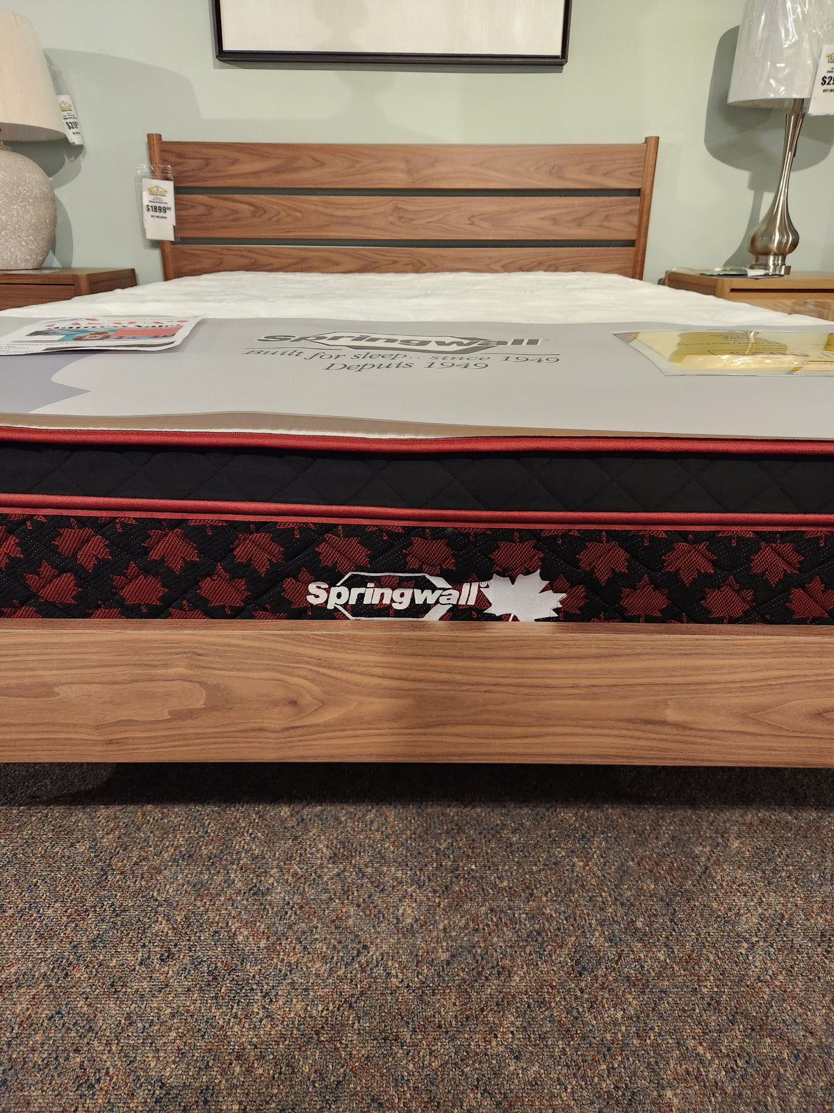 A Springwall Canada Day Mattress by Springwall is displayed on a wooden bed frame in a showroom.
