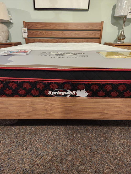 A Springwall Canada Day Mattress by Springwall is displayed on a wooden bed frame in a showroom.