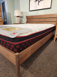 A Springwall Canada Day Mattress with a maple leaf pattern is shown on a wooden bed frame in a showroom.