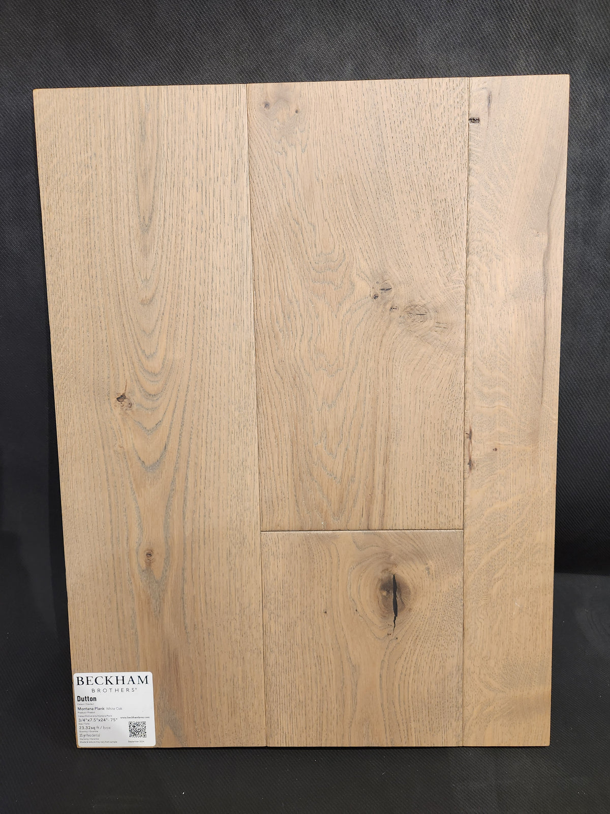 A display of Beckham Brothers’ Montana Plank White Oak flooring with visible grain, knots, and a label in the corner.