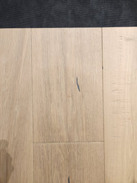 Montana Plank White Oak by Beckham Brothers: light-toned oak flooring with grain, small dark marks, and a dark top edge.