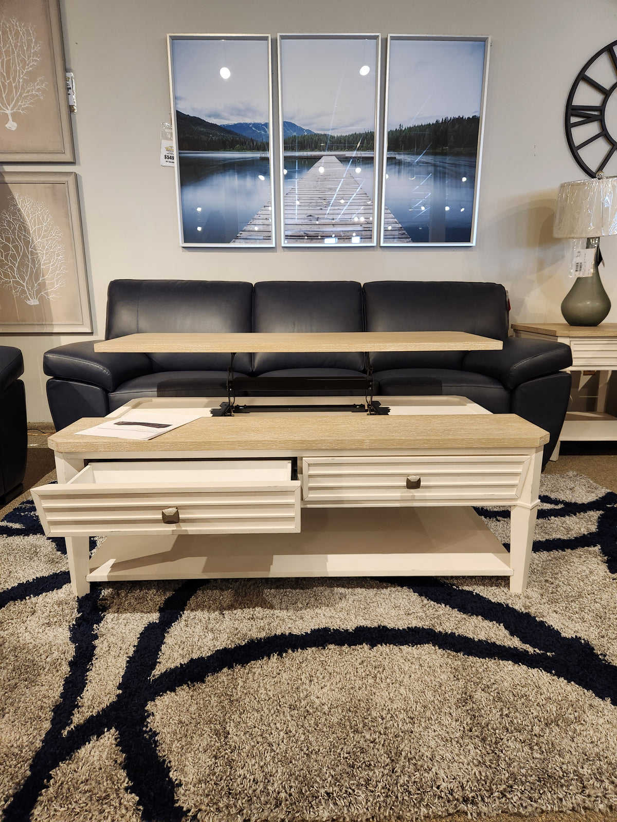A transitional casual living room with a navy sofa, Magnussen T6310-Echo Isles table, and landscape wall art.