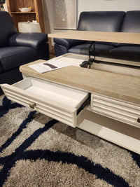 The Magnussen T6310-Echo Isles Lift Top Storage Cocktail Table sits on a gray rug between two blue sofas.