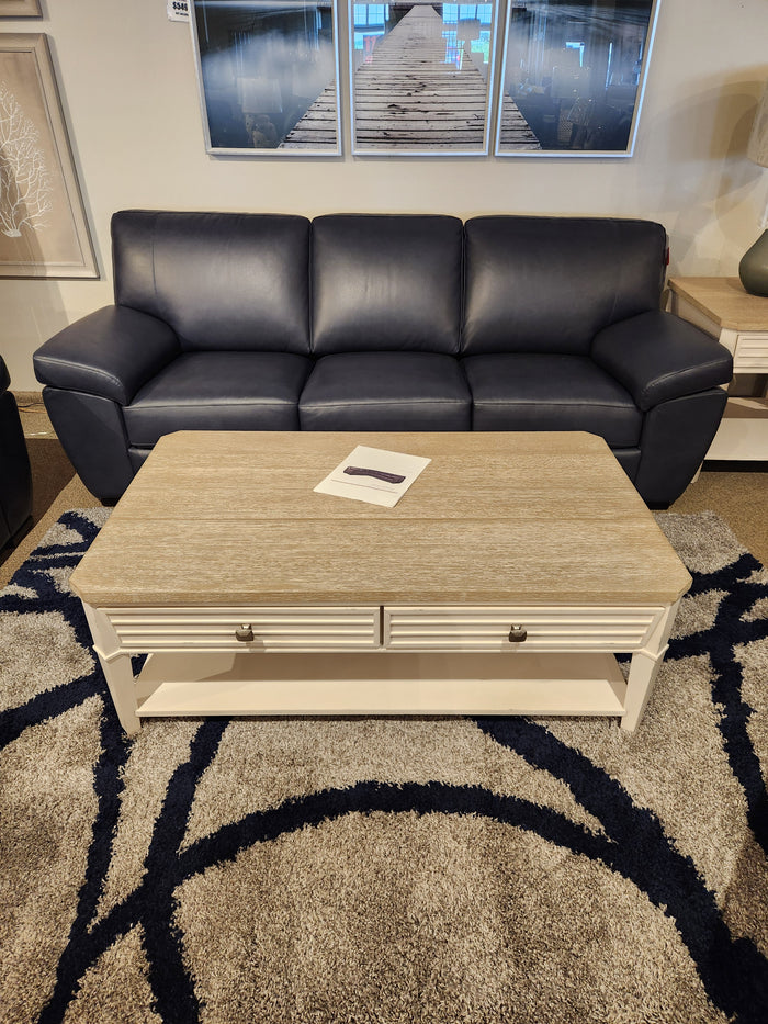 A dark blue leather sofa and Magnussen T6310-Echo Isles cocktail table rest on a patterned rug in transitional style.