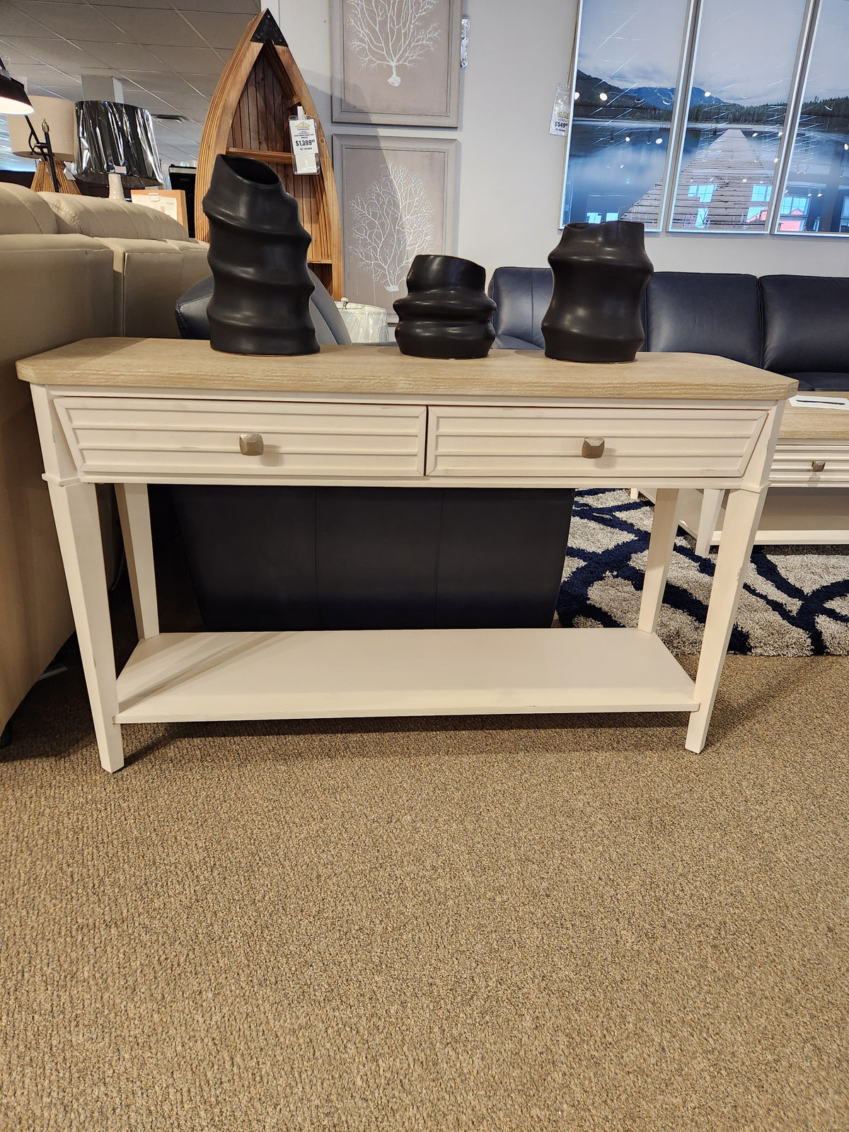 The Magnussen T6310-Echo Isles Sofa Table in white wood with oak top and 2 drawers, shown in a showroom.
