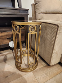 The Magnussen T6300 Lorena Round Accent Table with a brass finish sits by a beige sofa on a wooden floor.