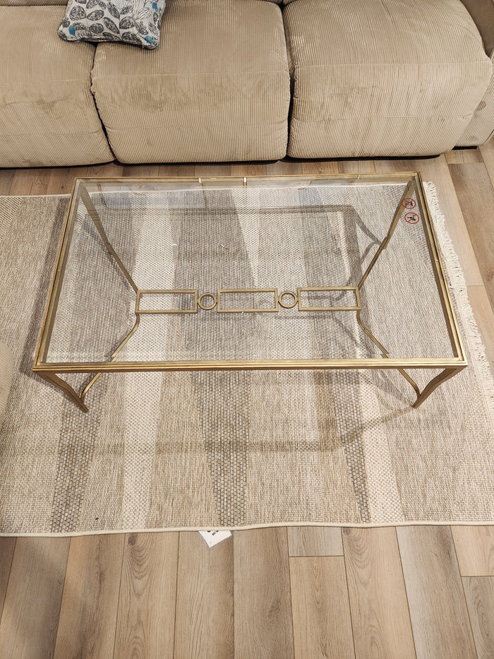The Magnussen T6300 - Lorena Cocktail Table with burnished brass finish sits on a striped rug before a beige sofa.