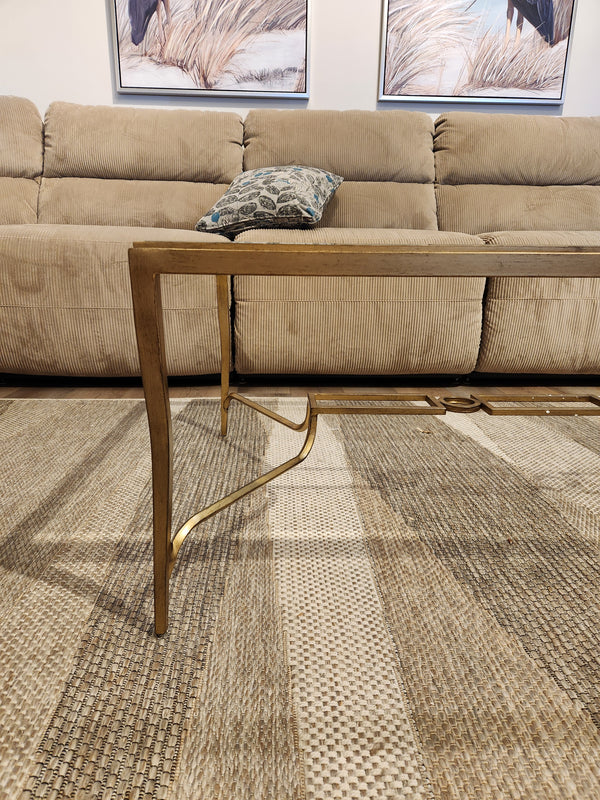 The Magnussen T6300 Lorena Cocktail Table with a burnished brass finish sits on a patterned rug before a tan sofa.