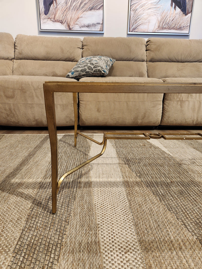 The Magnussen T6300 Lorena Cocktail Table with a burnished brass finish sits on a patterned rug before a tan sofa.
