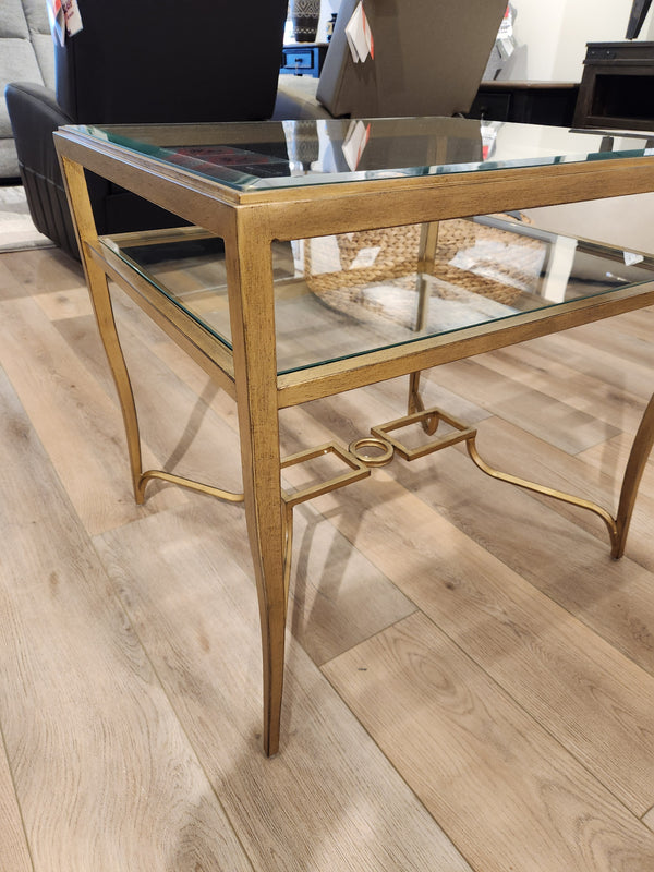 The Magnussen T6300 - Lorena End Table, with a brass finish, stands out on a light wood floor in the showroom.