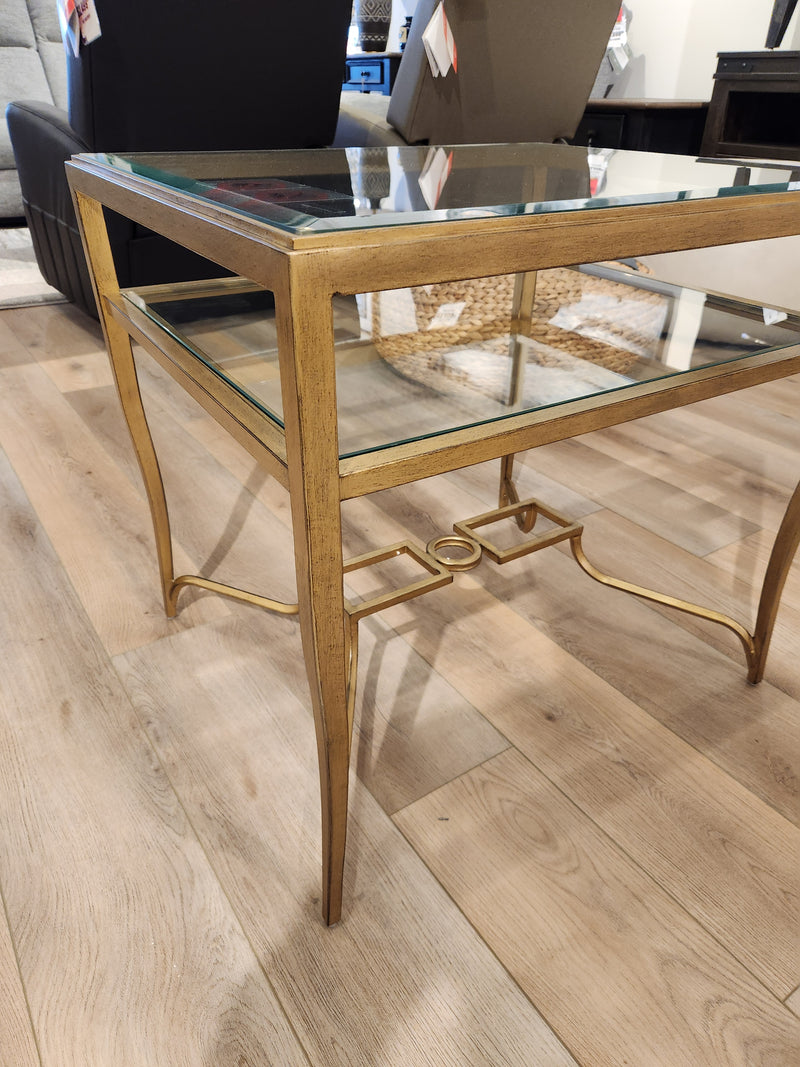 The Magnussen T6300 - Lorena End Table, with a brass finish, stands out on a light wood floor in the showroom.