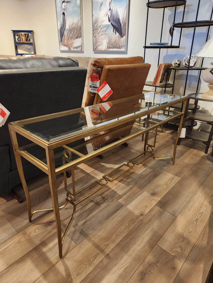 The Magnussen T6300 Lorena Sofa Table, featuring a glass top and brass finish, is showcased in the showroom.