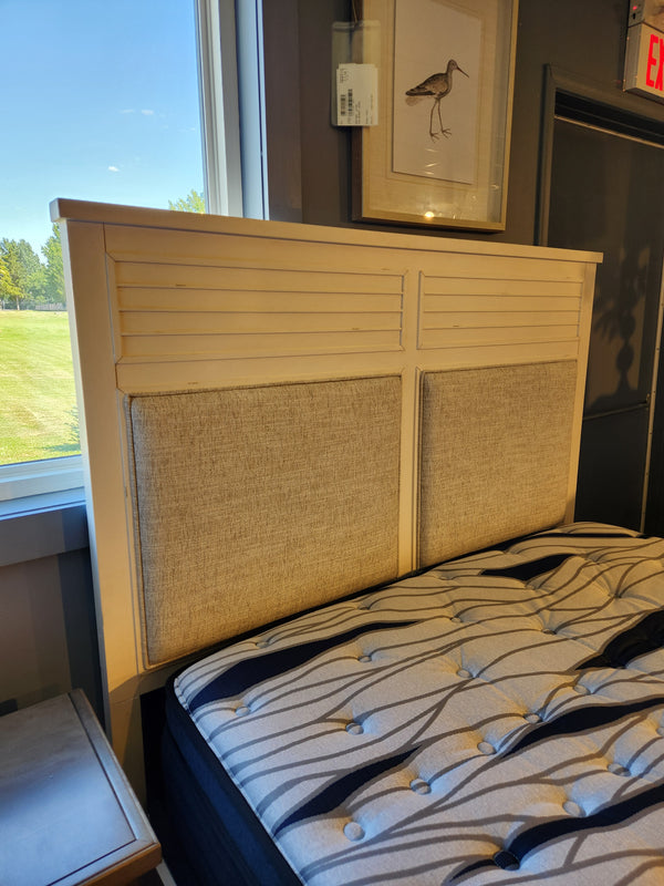 The B6310 - Echo Isles Bed by Magnussen features a cushioned headboard in transitional casual style, beside a window.