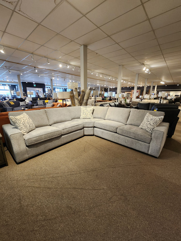 Decor-rest 2456 3-Piece Sectional in light grey with patterned pillows, shown on carpeted showroom floor under lights.