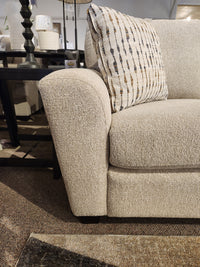 Beige Superstyle 5101 Sofa with a patterned pillow, black side table, lamp, on a brown carpeted floor.