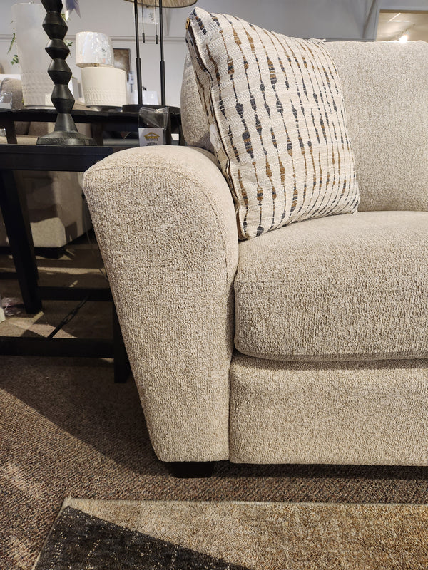Beige Superstyle 5101 Sofa with a patterned pillow, black side table, lamp, on a brown carpeted floor.
