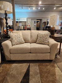 The Superstyle 5101 Loveseat comes with two patterned pillows, shown in a showroom with lamps and tables.